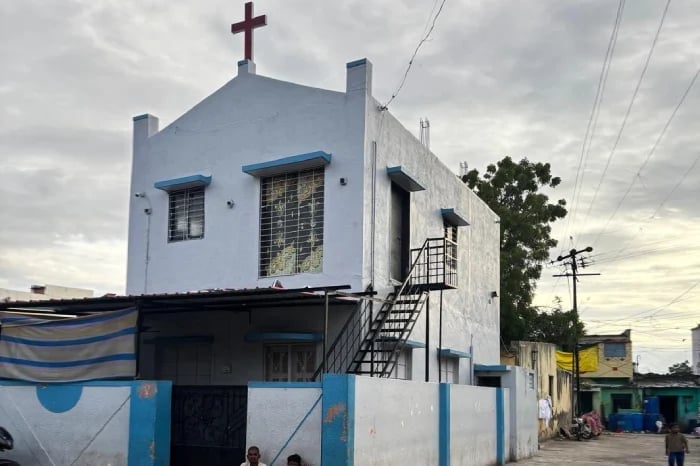White and blue two-storey church-like building with a cross, barred windows and external stairs in Bapuji Nagar, Solapur, linked to municipal probe.