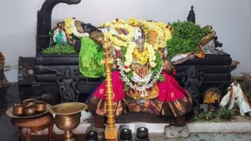 Garlanded temple deity on a black stone altar with brass lamps and ritual vessels, evoking Sri Rangam and Sri Ranganathaswamy devotion in a Vaishnava travelogue.