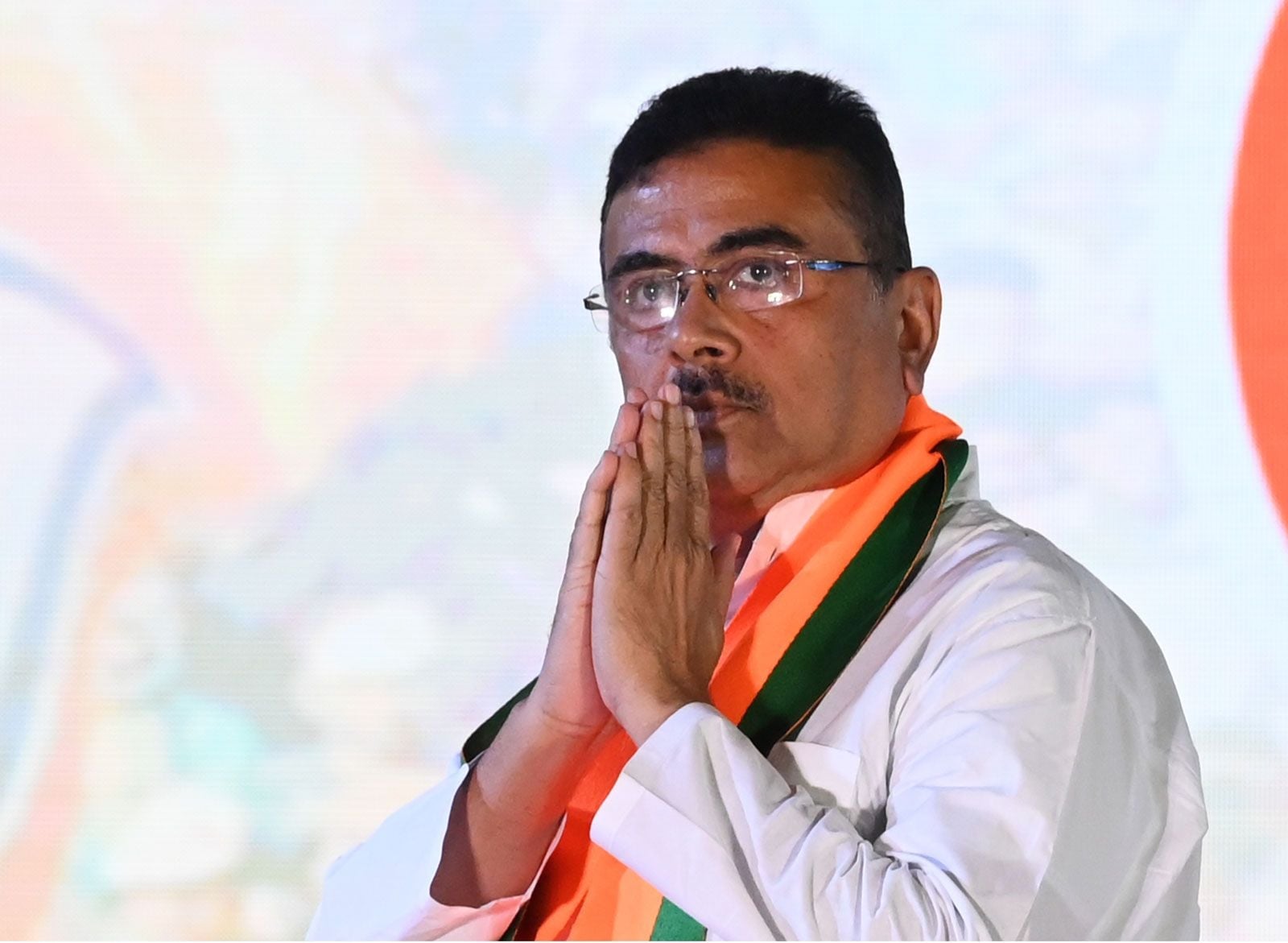 BJP नेता शुभेंदु अधिकारी सफेद कुर्ता और भगवा-हरे दुपट्टे में हाथ जोड़कर मंच पर दिख रहे हैं; Hindi Bharat UCC और Hindu Dharma संदर्भ।