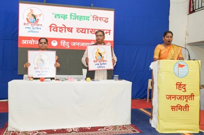 Women at a Hindu Janajagruti Samiti event hold Beti Surakshit, Rashtra Surakshit placards beside a podium during an Ichalkaranji awareness lecture.