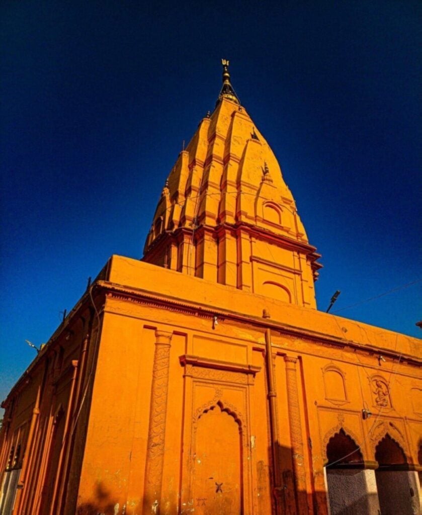 Saffron-orange Prithvinath Temple shikhara in Gonda, Uttar Pradesh, rising against a deep blue sky, highlighting Hindu Dharma travel heritage in Bharat