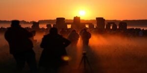 Silhouetted visitors and tripods watch sunrise over Stonehenge, a symbolic image for Ram Siya Ram prayers and Venezuela earthquake humanitarian aid.