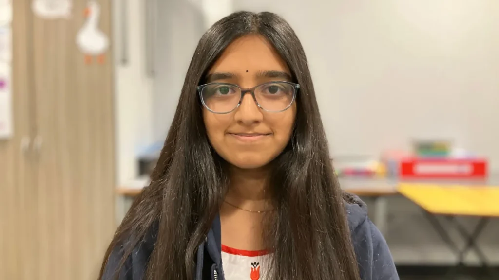 Young Hindu woman with glasses and a bindi in an indoor setting, illustrating World and Bharat concerns over youth culture and worship access.