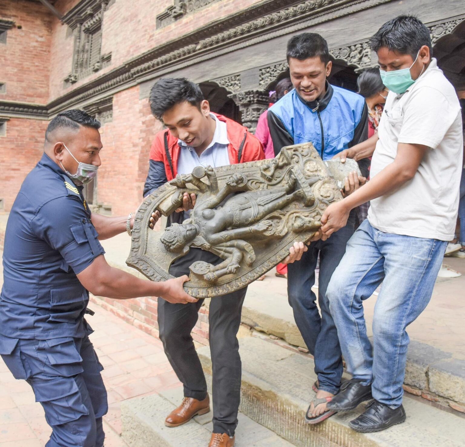 Men carry a carved Hindu deity relief in a Kathmandu heritage courtyard, reflecting Nepal’s sacred art, Hindu Dharma, Bharat ties, and World heritage.