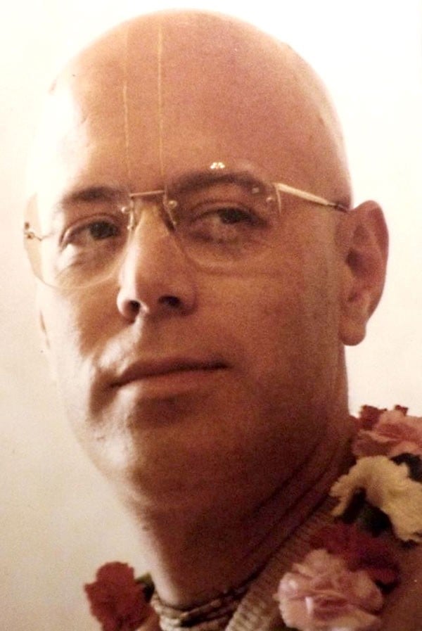 Close-up portrait of HH Tamal Krishna Goswami wearing glasses, tilaka, and flower garlands, connected to Bhakti Charu Swami's ISKCON remembrance