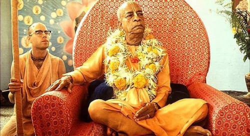 Srila Prabhupada sits garlanded in saffron robes on an ornate red chair, with a disciple nearby, reflecting ISKCON service and mission to China.