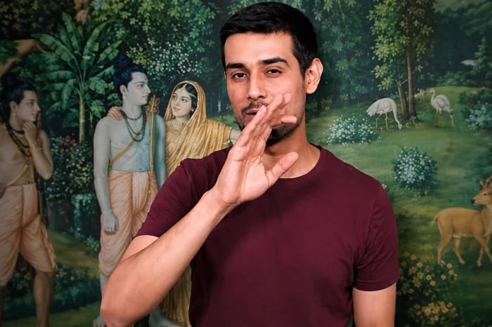 A man in a maroon T-shirt gestures before a Hindu devotional mural of Rama, Sita and Lakshman, used with HJS love jihad awareness coverage.