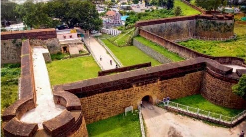 Aerial view of Devanahalli Fort in Bharat, showing ancient stone walls, an arched gateway, green lawns and pathways linked to Hindu Dharma history.