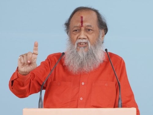Elderly bearded speaker in saffron clothing gestures at a podium, used with news on the Taj Mahal Tejomahalaya High Court petition.