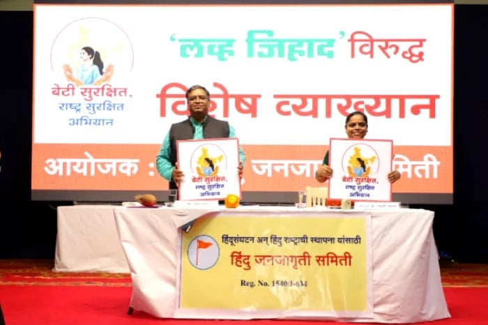 Two Hindu Janajagruti Samiti speakers on stage holding Beti Surakshit campaign placards before a Hindi Love Jihad awareness lecture banner.