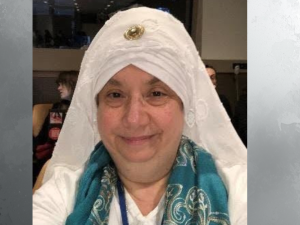 Smiling Sikh woman wearing a white head covering and teal scarf indoors, accompanying a SikhNet article on Bhai Mani Singh's enduring legacy.