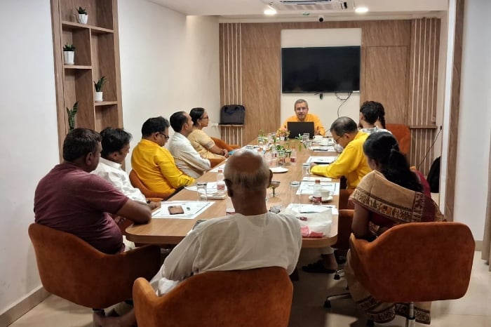 Meeting room discussion on Goa Government temple renovation contract issue, with attendees seated around a conference table and a speaker at the front