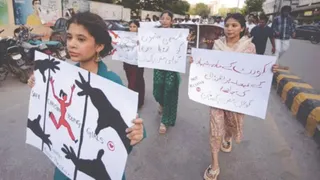 पाकिस्तान में अल्पसंख्यक महिलाओं पर हिंसा के विरोध में सड़क पर तख्तियां लेकर प्रदर्शन करती युवतियां, आगे पोस्टर थामे एक महिला।