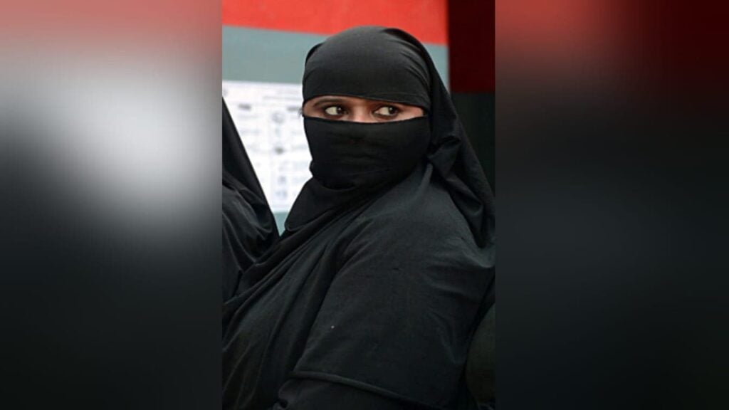 इनडोर स्थान पर काला नकाब और सिर ढकने वाला परिधान पहने महिला, केवल आंखें दिखाई दे रही हैं; मुजफ्फरनगर मदरसा आरोपों से जुड़ी सांकेतिक तस्वीर।