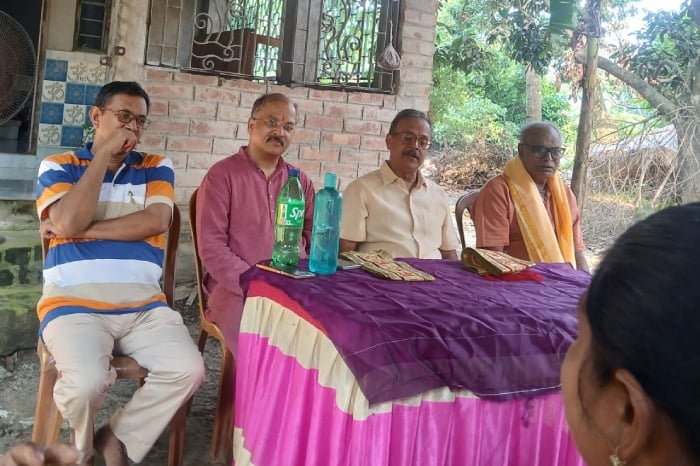 Four men sit beside a purple-covered table during a Hindu Rashtra-Jagruti meeting in North 24 Parganas, West Bengal, with an attendee in front.