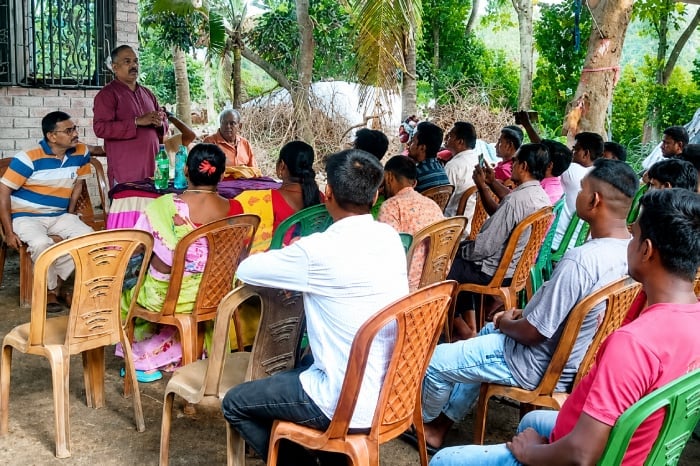 A speaker addresses men and women seated on plastic chairs at an outdoor Hindu Rashtra-Jagruti meeting in North 24 Parganas, West Bengal.