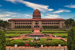 Front view of the National Defence Academy’s Sudan Block in Khadakwasla, Pune, framed by formal gardens beneath a blue sky.