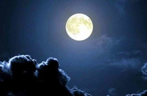Bright moon glowing in a deep blue night sky above dark, silver-edged clouds, illustrating Chandra Darshan in Shravan Month and its Vratas-Pujas.