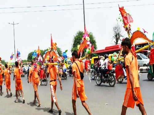 Kanvariyas in saffron clothing carry brightly decorated kanwars along a busy road during the Shravan Month pilgrimage to Deoghar Baidyanath Dham.