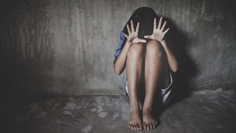 Illustrative image of a distressed child sitting against a bare concrete wall, knees drawn up and hands shielding their face, for a sexual assault report in Uttarakhand.