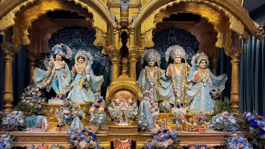 Ornately dressed Hindu deities in pale blue garments and flower garlands stand within a gilded altar at Bhaktivedanta Manor for ISKCON’s 60th anniversary.