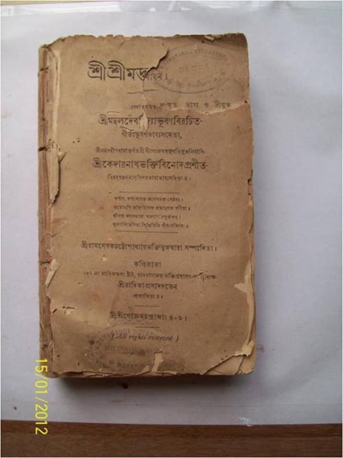 A worn brown Bengali-language book linked to Srila Bhaktivinoda Thakura, with a torn spine, frayed cover, faded script, and a 2012 date stamp.