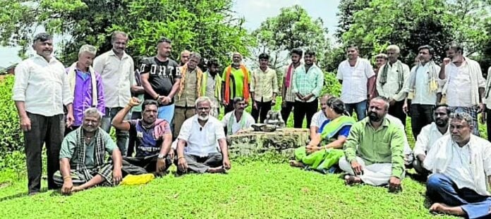 Villagers gather around a small stone shrine in a grassy clearing in Amblikoppa, Dharwad, Karnataka, after the reported Beeralingeshwara murti vandalism.