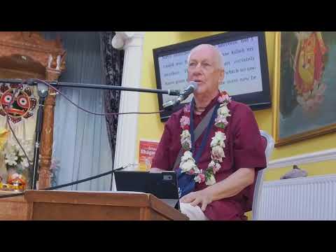 HG Vaiyasaki Dasa, wearing a flower garland, speaks into a microphone from a temple lectern during a Srimad Bhagavatam 8.19.11–12 class.