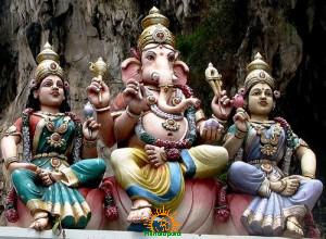 Lord Ganesha sits between Siddhi and Buddhi in an ornate cave shrine tableau, illustrating a traditional marriage story for Ganesh Chaturthi.