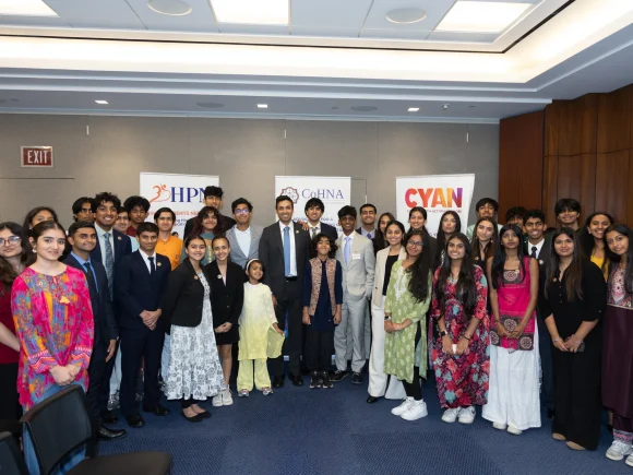 Large group of adults and children posing together in a conference room beneath organization signs.