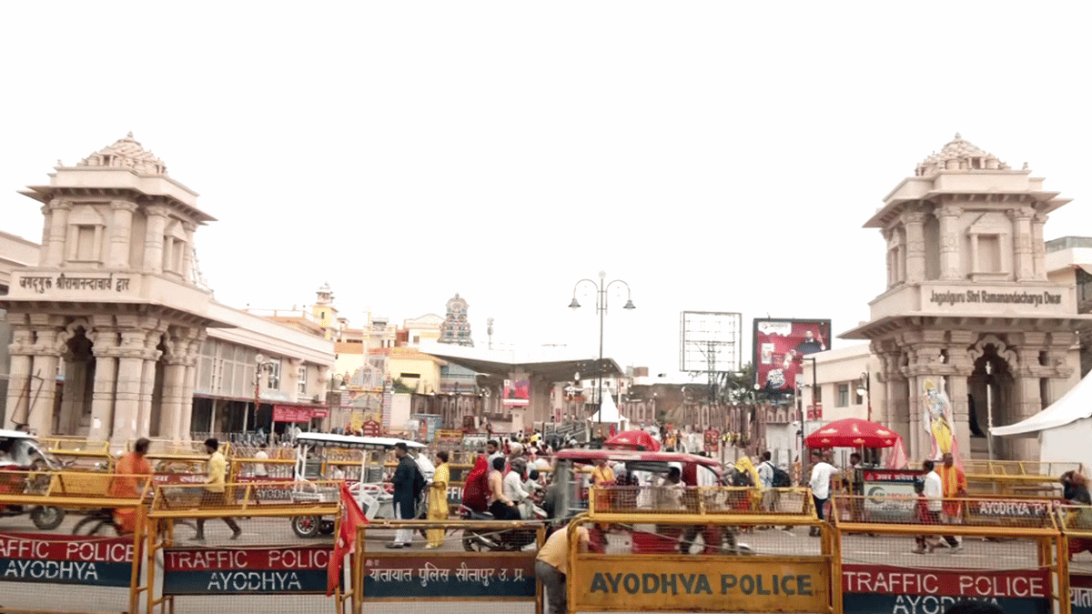 Crowds and vehicles behind Ayodhya Police barricades between two ornate gateway towers.