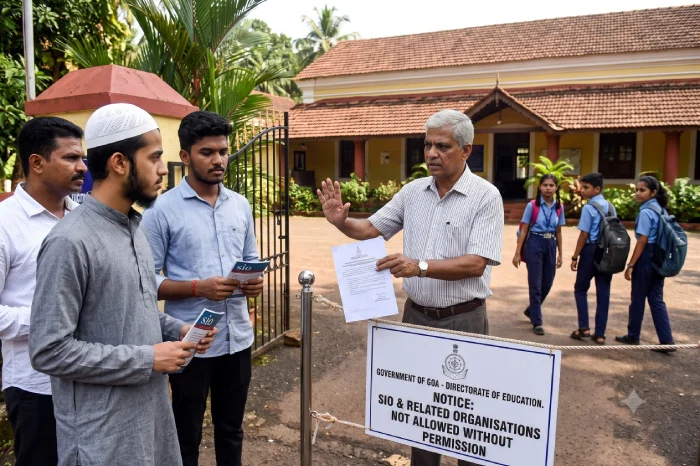 Man holding a document speaks to three men beside a notice restricting SIO and related organisations.