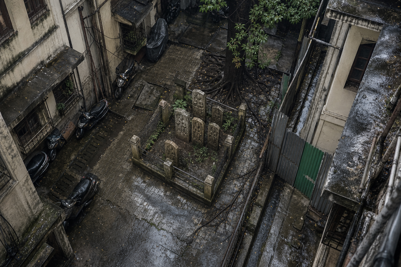 An intact group of hero stones occupies a small enclosure crowded by apartment walls, paving, utilities, vehicles, and rainwater runoff.