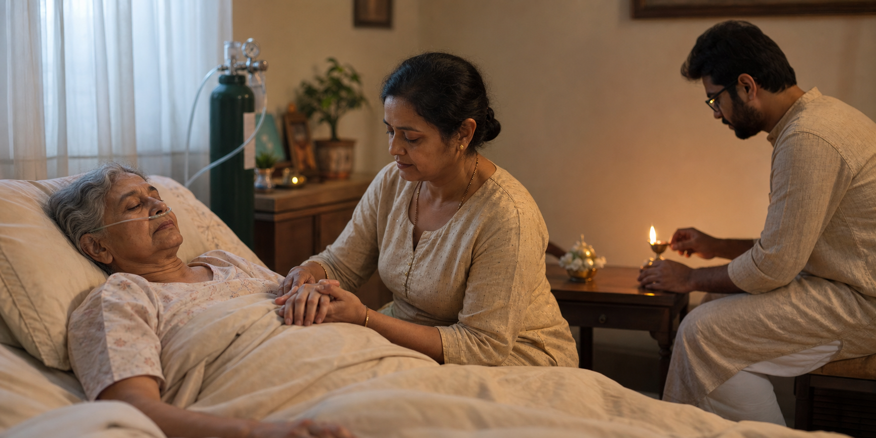 An elderly Indian patient rests in bed while one relative holds their hand and another tends a small oil lamp nearby.