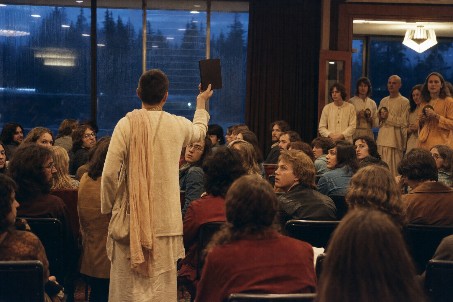 A devotee holding a plain-covered book draws the attention of concertgoers in a rainy Vancouver venue in 1974.