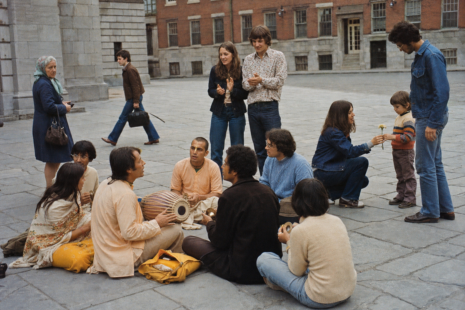 Devotees perform kirtan in a Montreal public square as some passersby clap, one child receives a flower and others watch or walk away.
