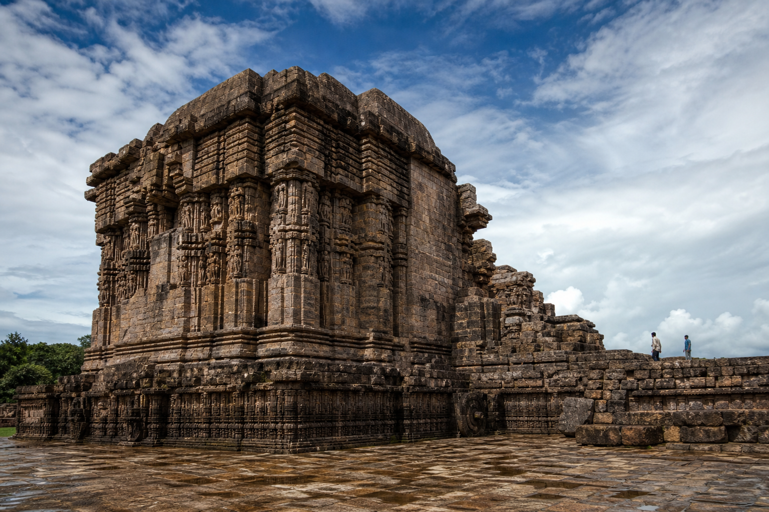 Side view of the massive surviving temple hall and ruined masonry at Konark, showing weathered stone courses, carved wall zones, and broken structural edges.