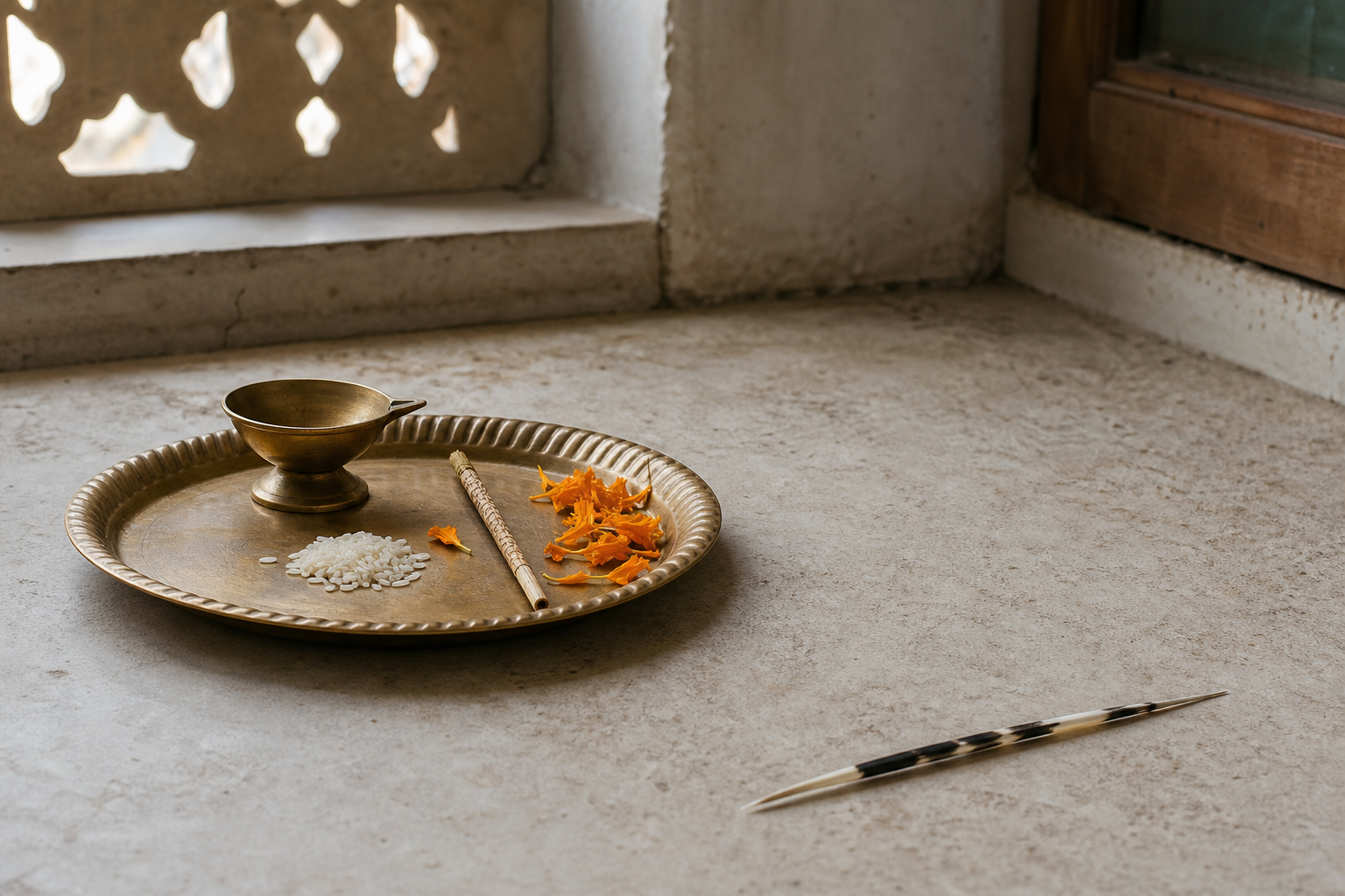 A patterned porcupine quill rests beside, but separate from, a brass puja tray with a lamp, marigold petals, rice, and a reed implement.