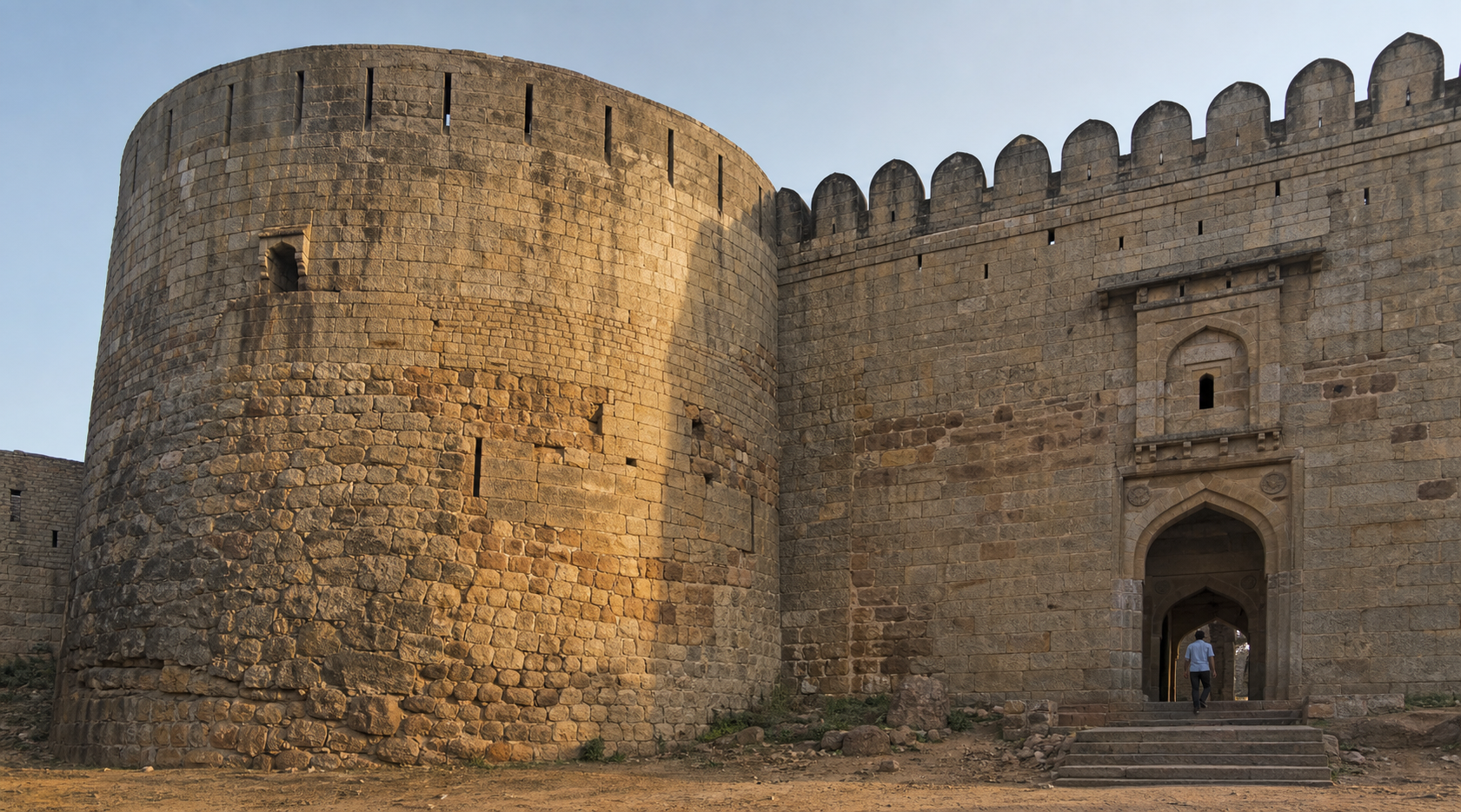 Weathered masonry, repairs and altered openings are visible across a bastion and gateway wall at Devanahalli Fort.