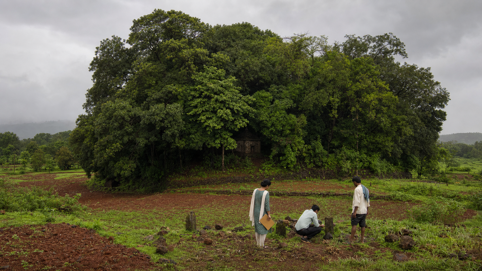 Field investigators and a local custodian observe a dense sacred grove and small stone shrine amid Konkan farmland.