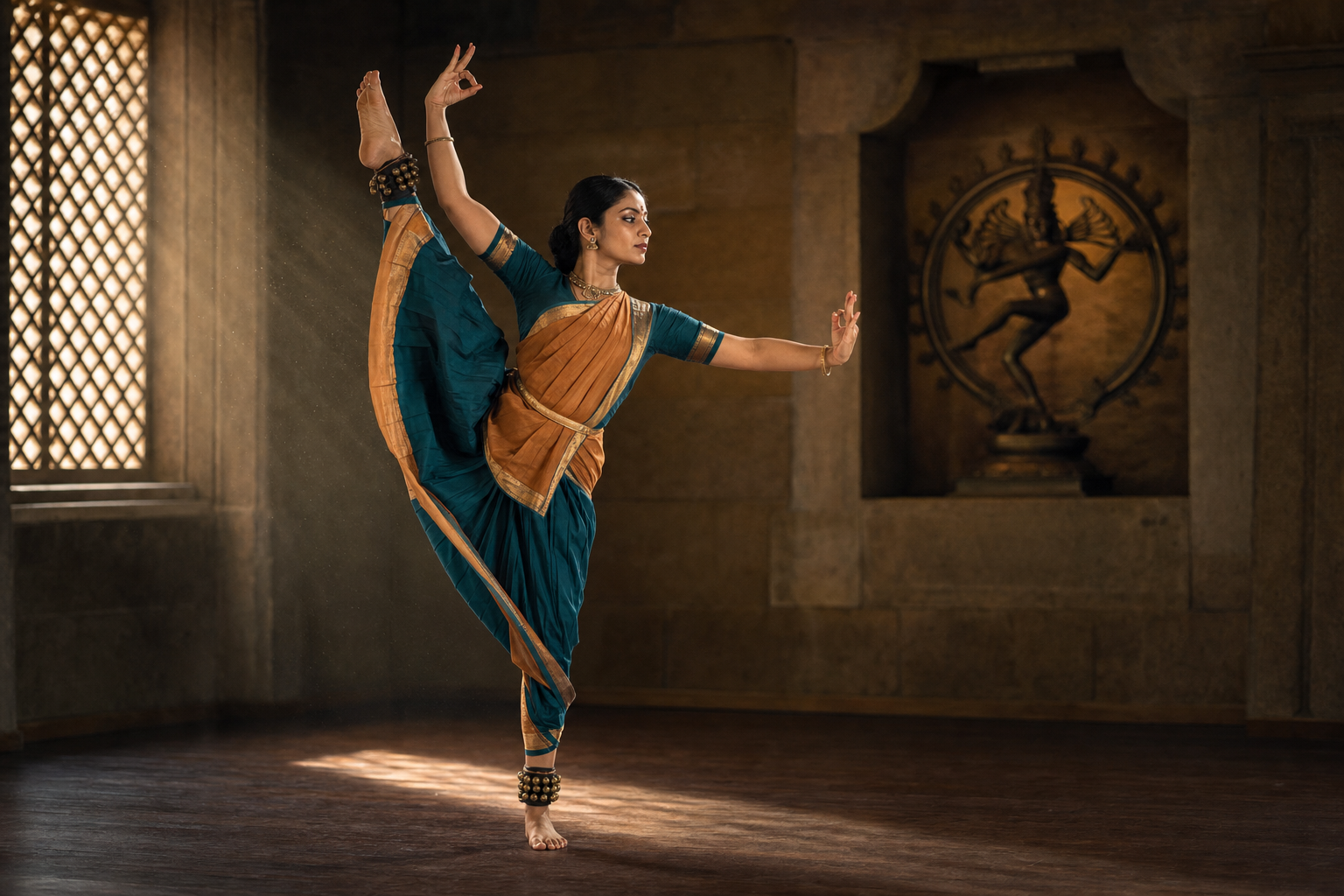 An Indian classical dancer practices a high lifted-leg pose in a quiet stone rehearsal space with a dancing Shiva figure in a background niche.
