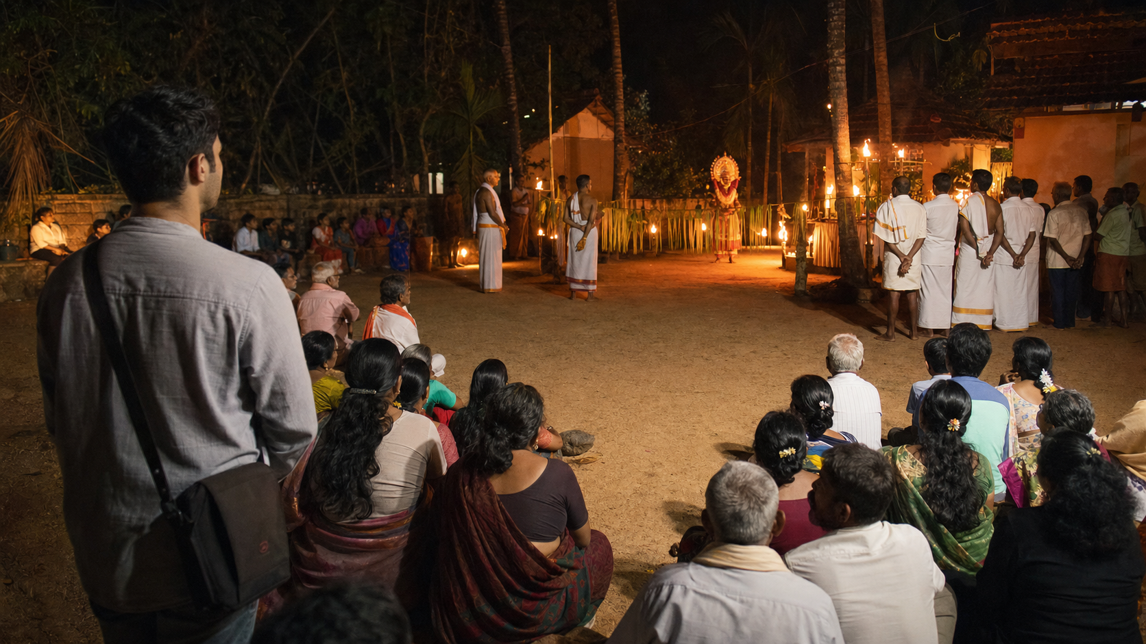 Community members watch a torchlit Bhuta Kola from a respectful distance while a visitor keeps a phone inside a bag and leaves the ritual path clear.