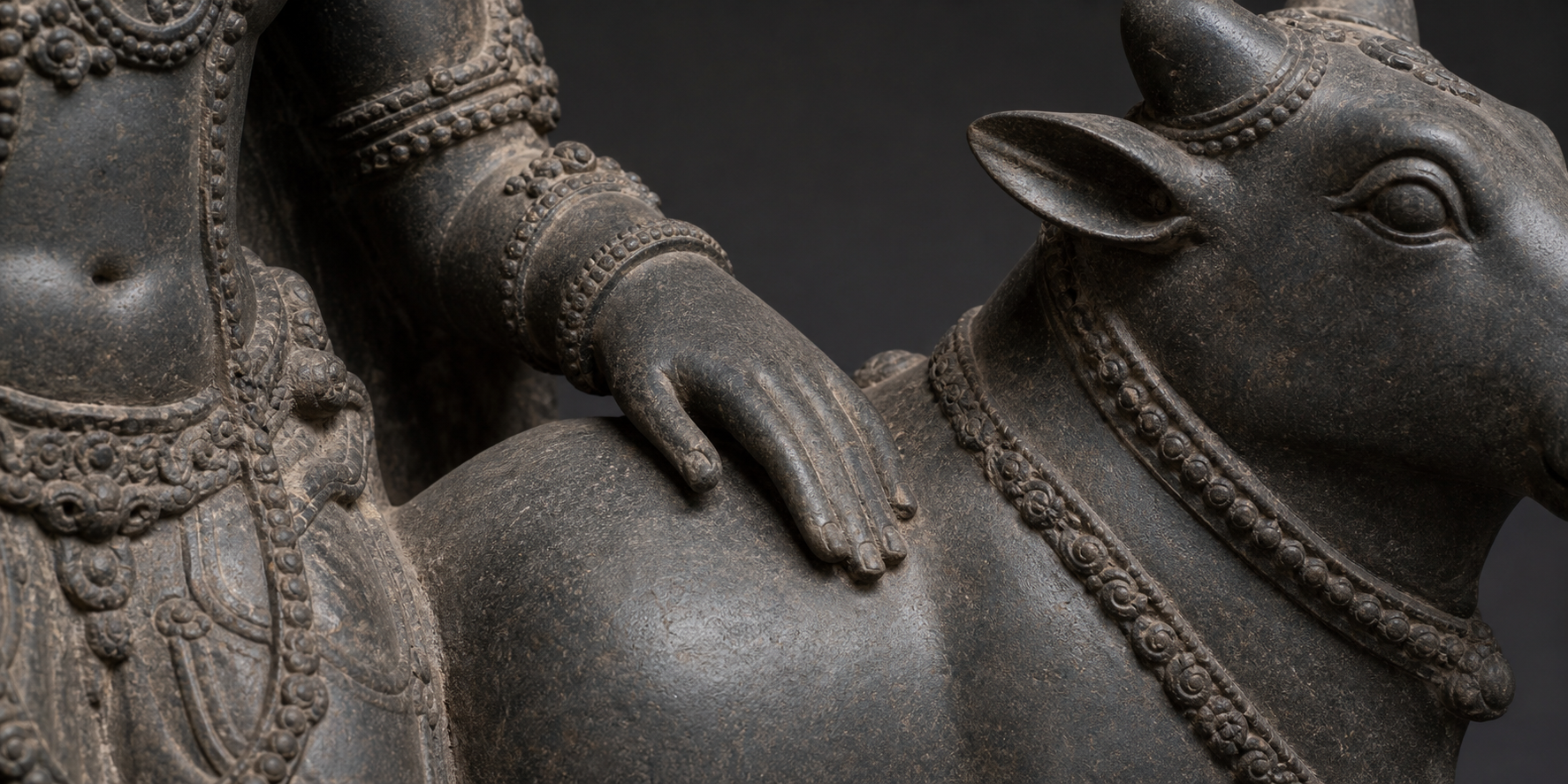 Close view of a carved Shiva figure's ornamented arm resting across the back of Nandi.