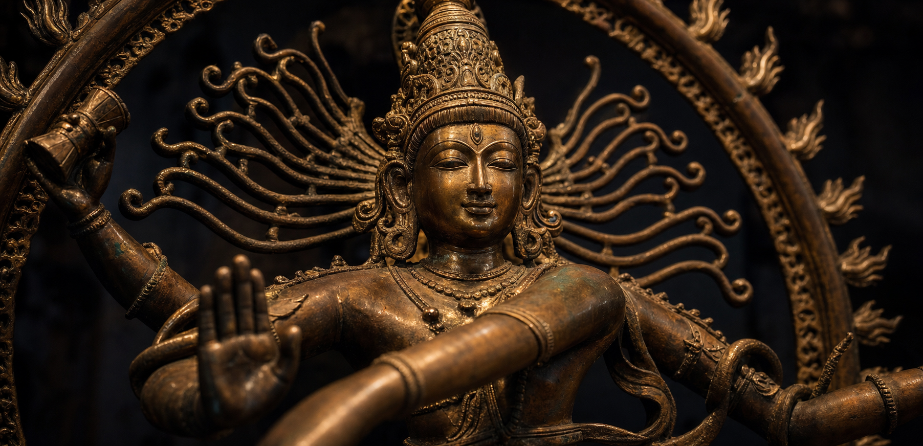 Close view of Shiva Nataraja's serene face and upper body framed by outward-flying hair, flames, an open palm, and a small drum.