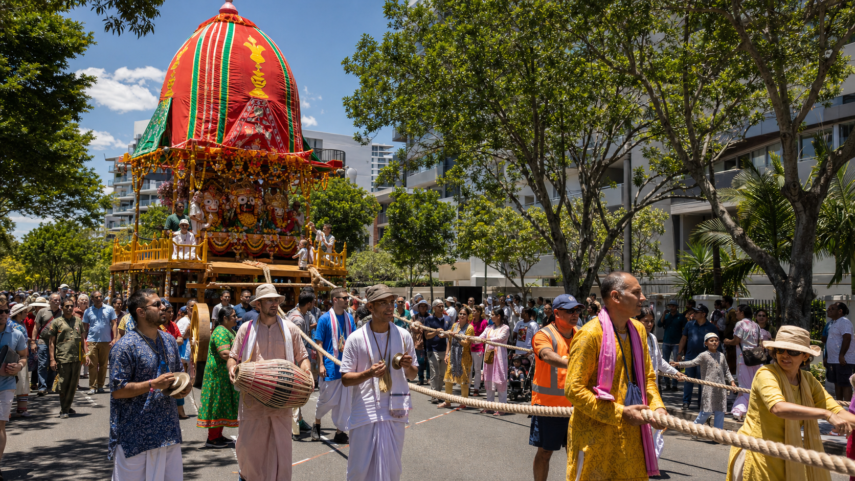 A diverse crowd walks beside a brightly canopied Ratha Yatra chariot during a sunny street procession in Brisbane.