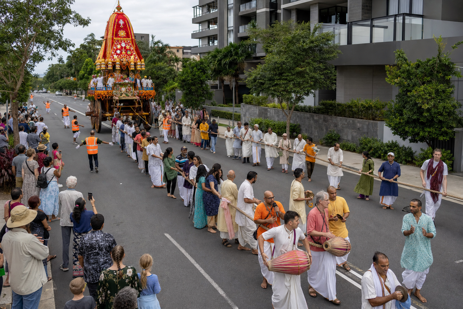 Participants pull long ropes in front of a decorated chariot while musicians, stewards and spectators move through an orderly street procession.