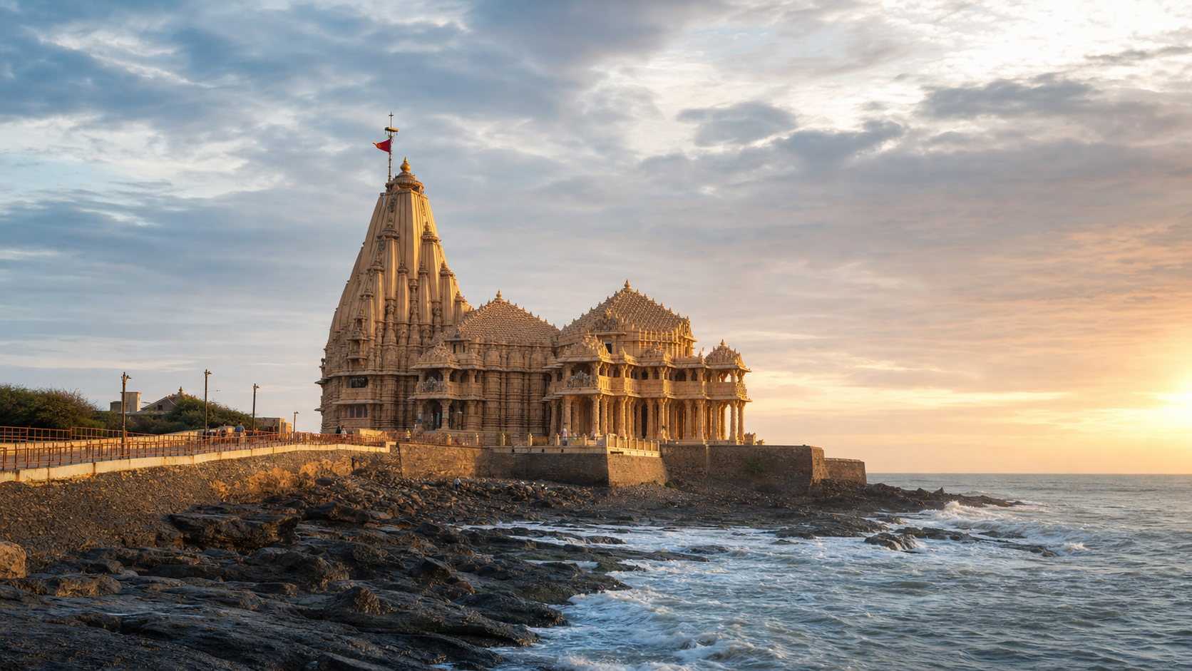 Somnath Temple illuminated by sunrise above the rocky Arabian Sea coast, with a few distant pilgrims approaching along the promenade.