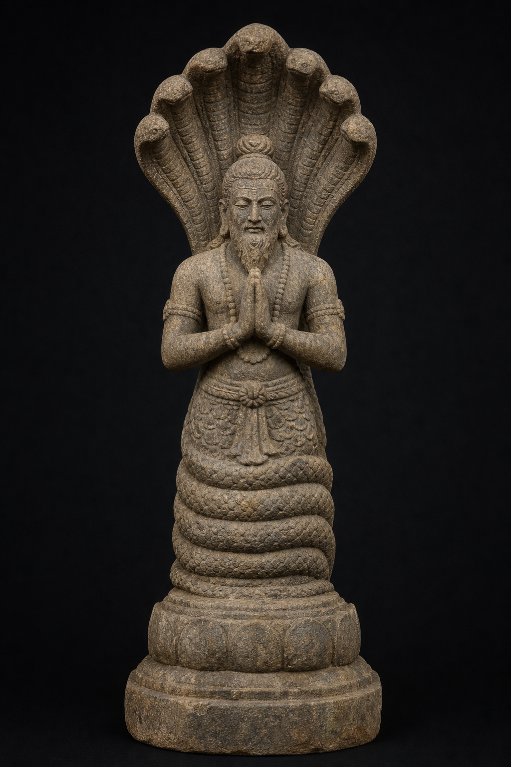 A weathered stone sculpture of a serene sage with folded hands, a coiled serpent lower body, and a multi-hooded cobra canopy.