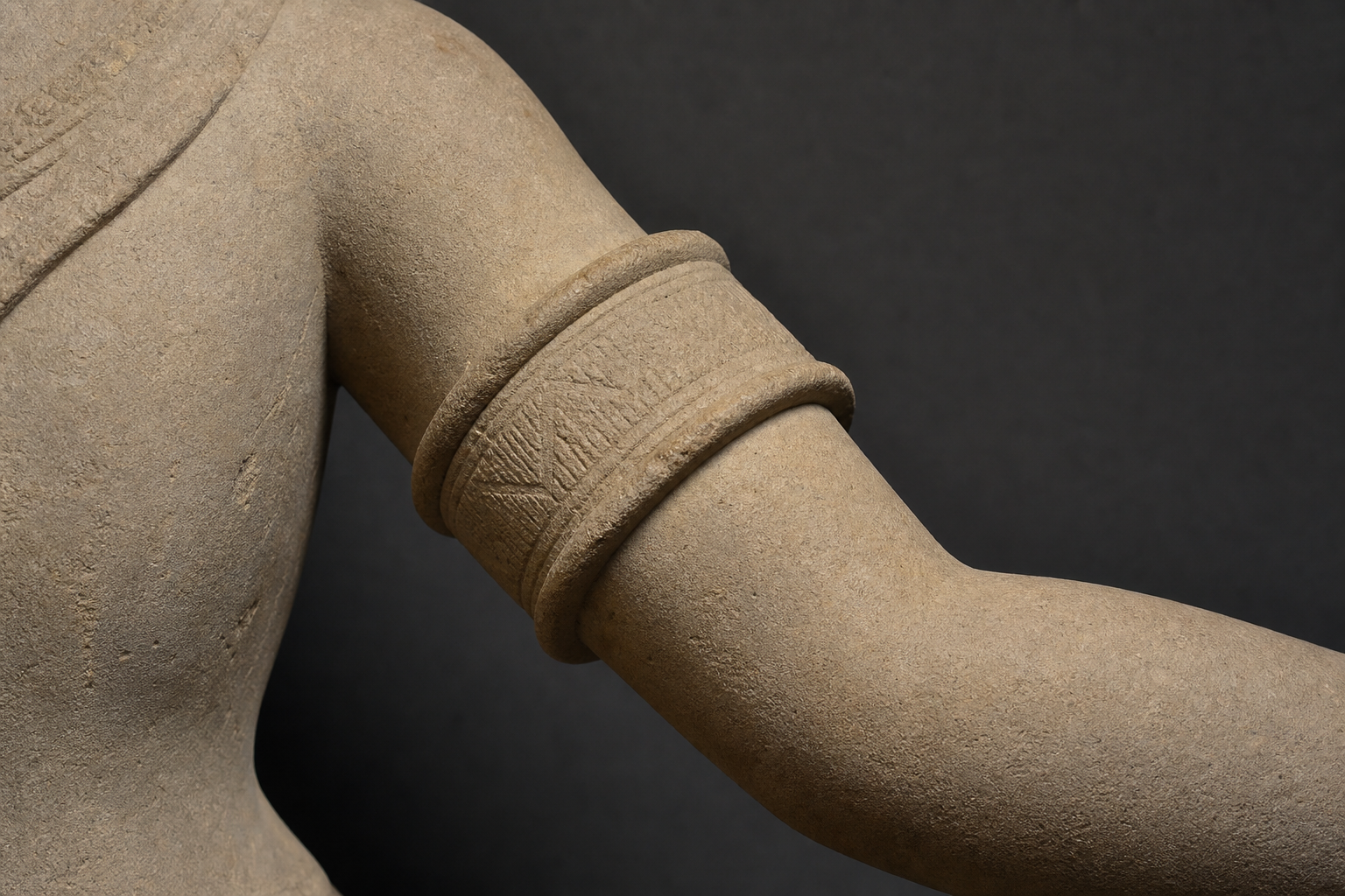 Close-up of a sandstone upper arm with a broad continuous cylindrical cuff positioned immediately above the elbow.