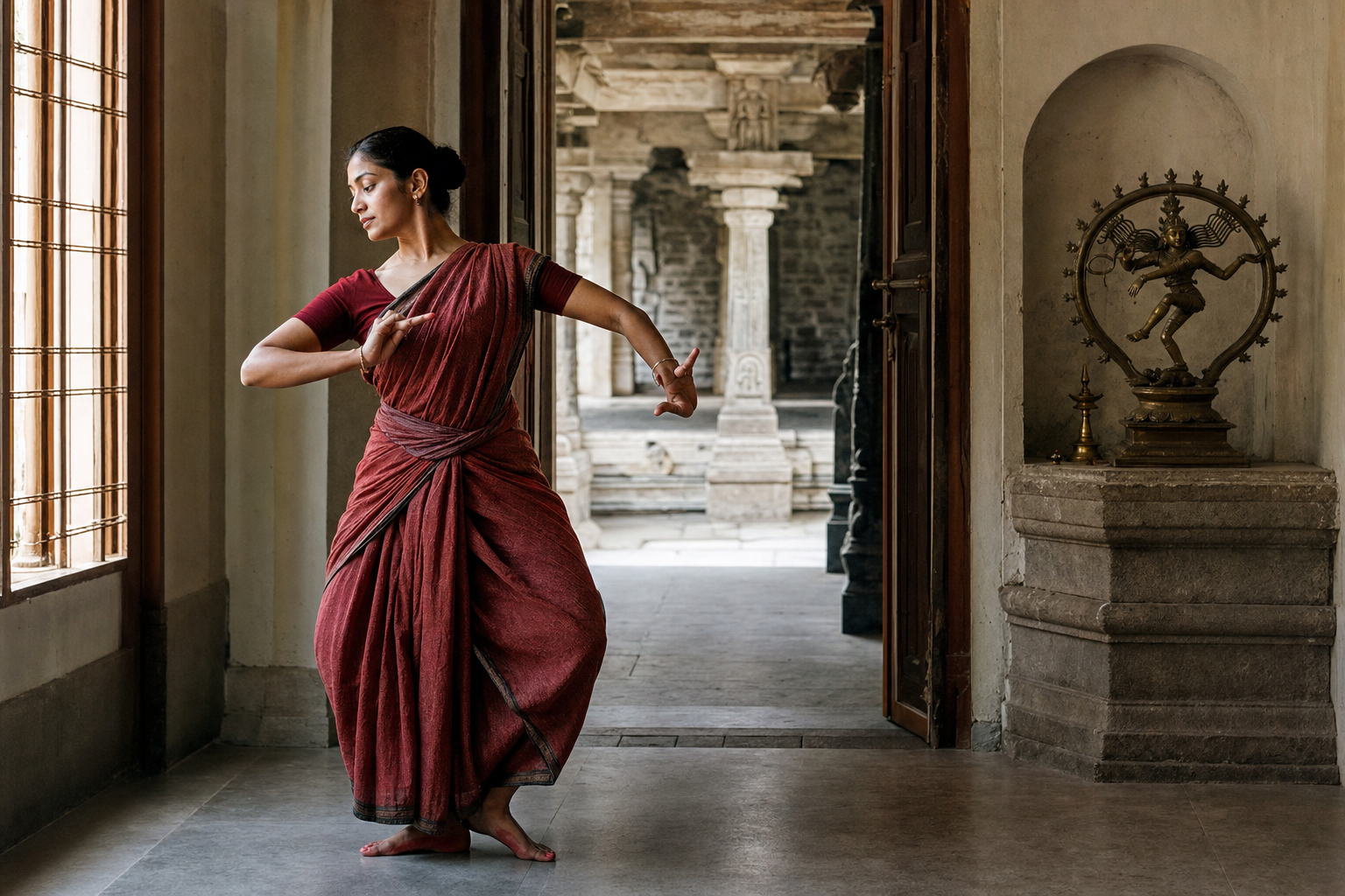 A contemporary Bharatanatyam dancer practices in a simple hall beside a small Shiva shrine, with an old temple corridor visible through the doorway.